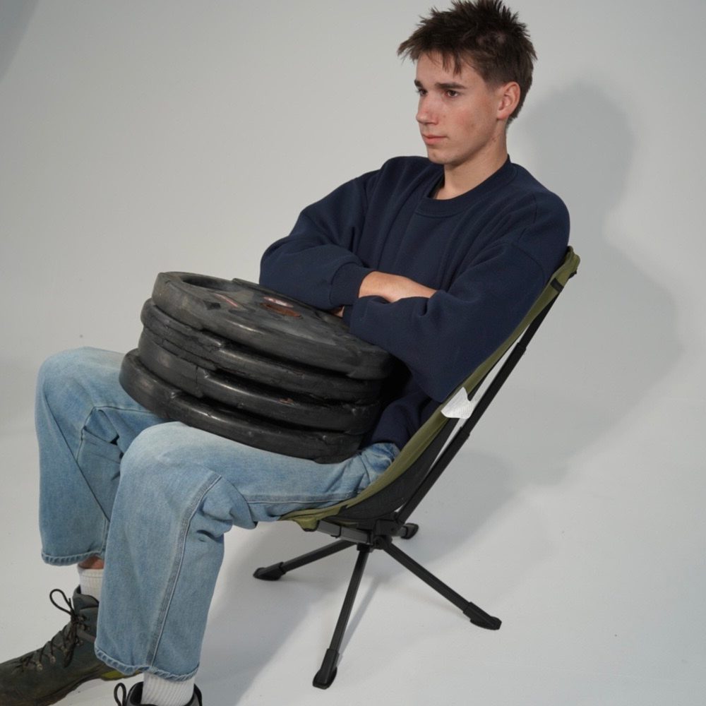 A seated man holding a stack of heavy weight plates in the Pacto chair